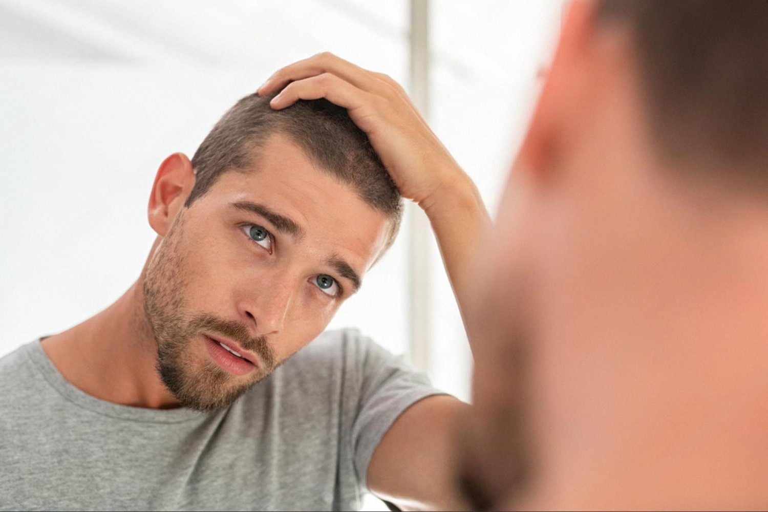 Young man in Dubai examining thinning hair in a bathroom mirror