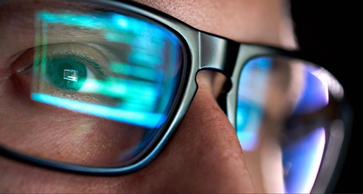 Close-up of glasses reflecting code, representing the technical decision of registering a .ae or .com domain